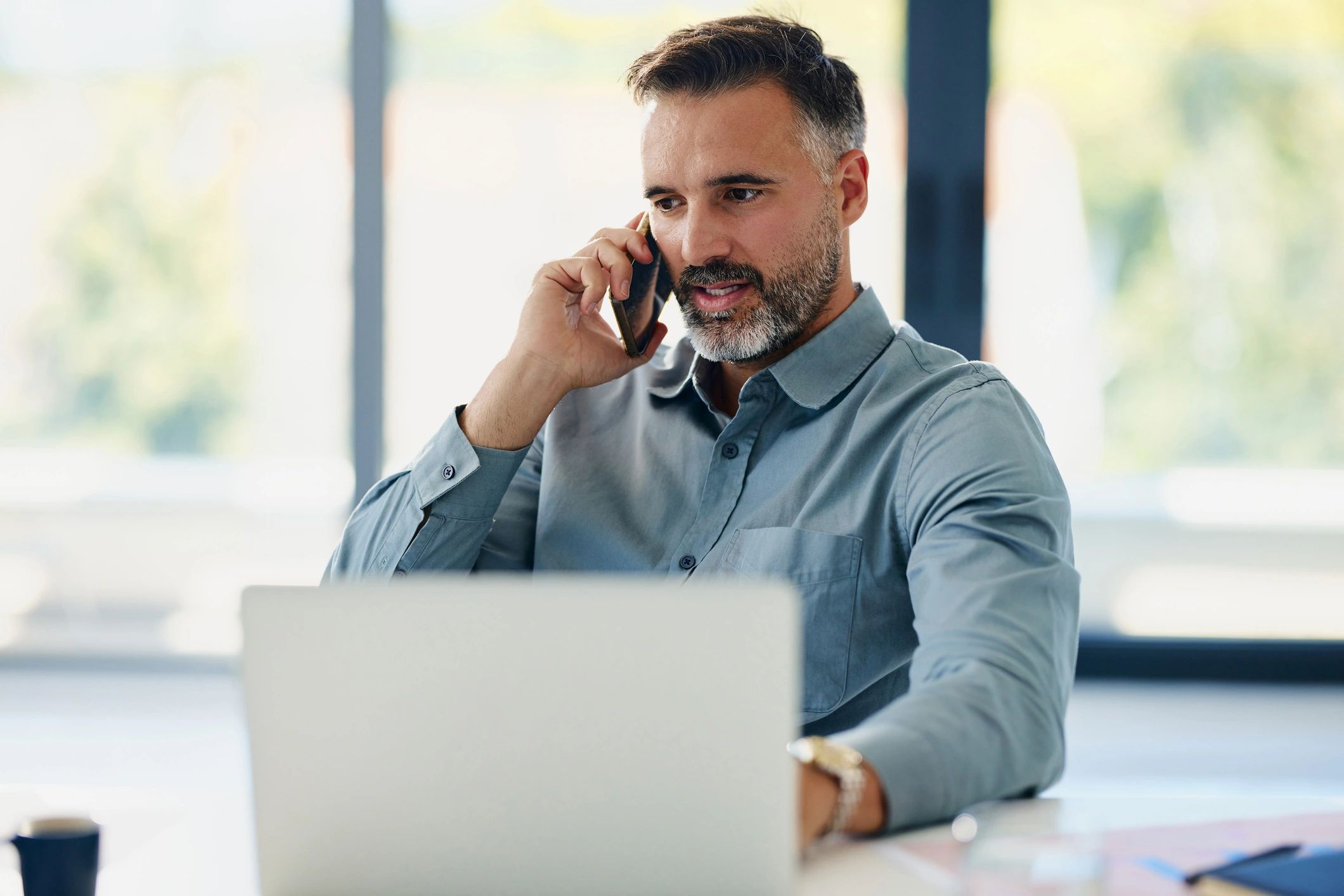 Person speaking on the phone while working at a laptop in an office.
